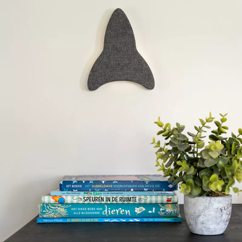 Sfeerbeeld van Ollie & Leila's Ollie's Rocketship, een grijs raketvormig nachtlampje en witte ruis machine, gemonteerd aan de muur boven een stapel kinderboeken en naast een plantje, als moderne kinderkamerdecoratie.